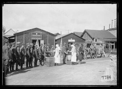 A line of Americans receiving sandwiches and coffee in front of the AMERICAN RED CROSS line-of-communicatio…
